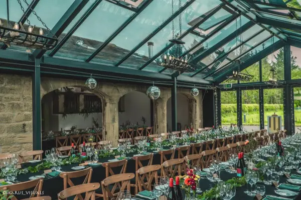 Elegant greenhouse reception area featuring wooden tables, chandeliers, and lush greenery, perfect for a romantic wedding celebration.