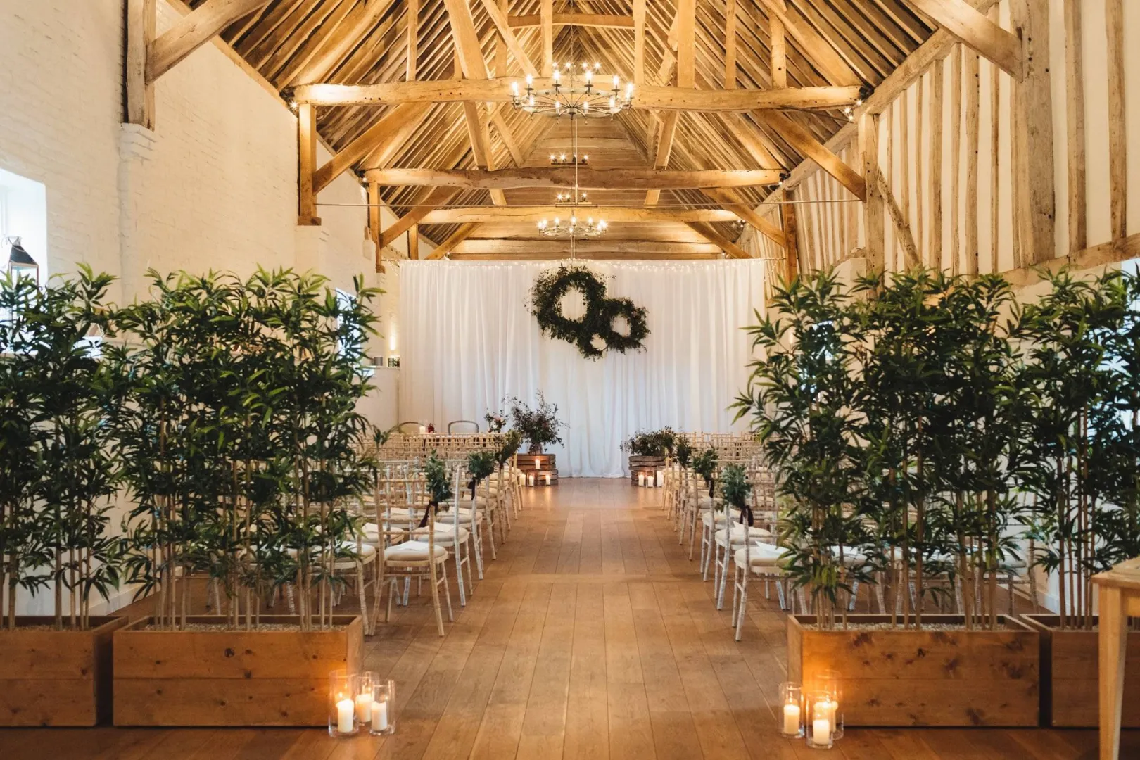 Rustic barn wedding venue featuring elegant wooden beams, lush greenery aisle markers, and softly glowing candles adorning the space.