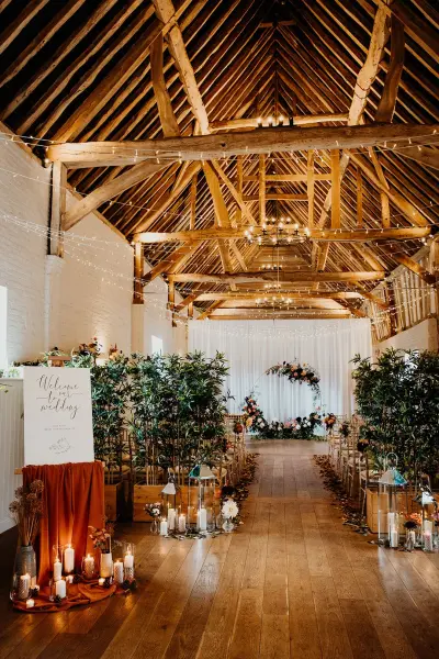 Rustic barn venue featuring exposed wooden beams, candle-lit aisle, lush greenery, and elegant decor for a charming wedding ceremony.