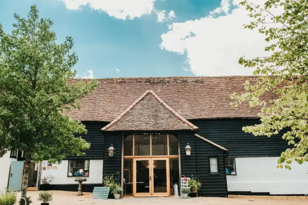 Charming rustic barn venue with a thatched roof, surrounded by lush greenery and a welcoming entrance, perfect for a picturesque wedding.