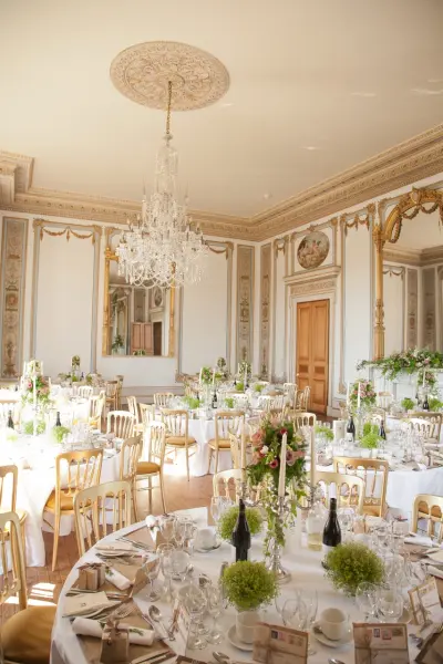 Elegant dining room with chandeliers, ornate mirrors, and beautifully set tables, featuring floral centerpieces and classic decor.
