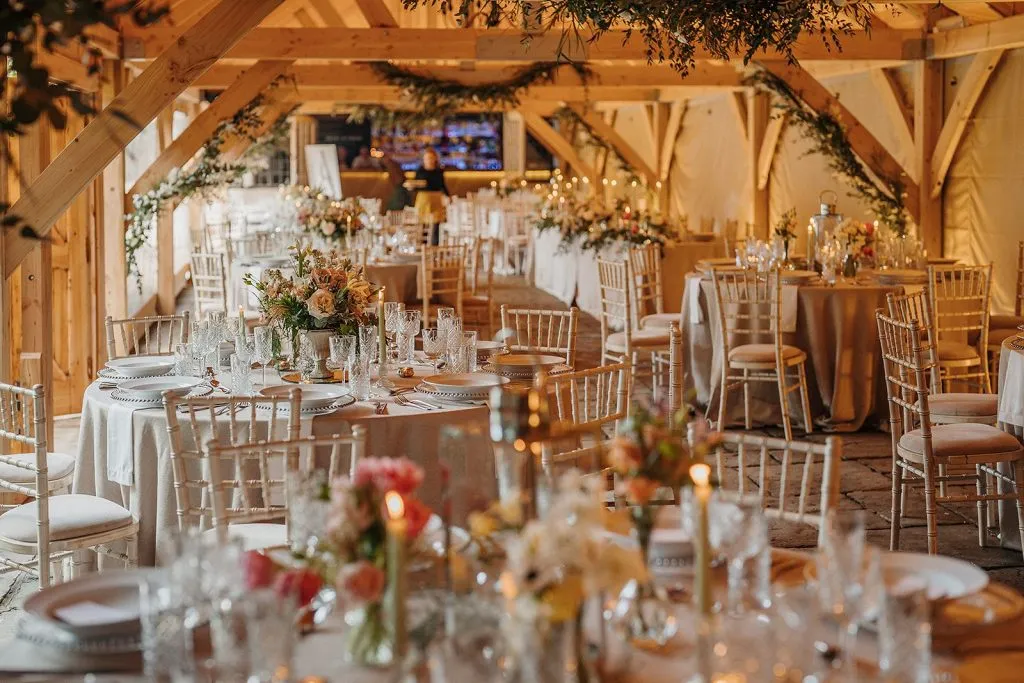 Elegant reception space featuring wooden beams, beautifully set tables, soft candlelight, and lush floral centerpieces for a romantic atmosphere.