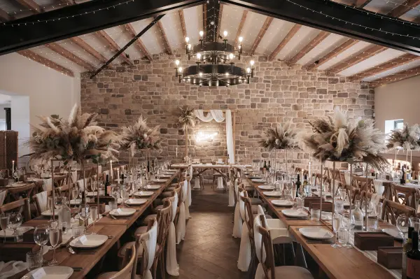 Elegant indoor reception space featuring rustic wooden tables, stone walls, and soft floral arrangements, perfect for a cozy wedding atmosphere.
