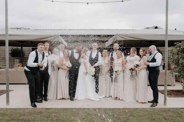 A joyful wedding party celebrating outdoors, surrounded by elegant tents and lush greenery, capturing a moment of cheer and togetherness.