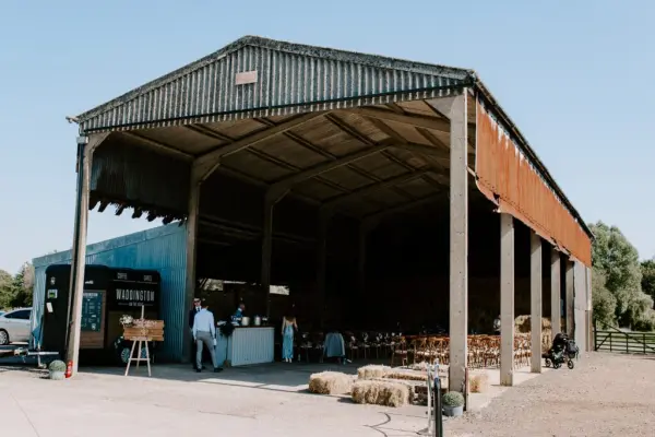 Spacious rustic barn with exposed beams, wooden seating, and open sides, ideal for a charming indoor-outdoor wedding celebration.