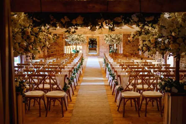 Charming rustic ceremony space with elegant wooden chairs, lush floral arrangements, and a lovely aisle leading to a decorated backdrop.