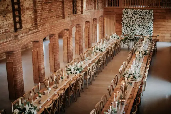 Rustic barn venue featuring long wooden tables adorned with candles and floral arrangements, set against a charming brick backdrop.
