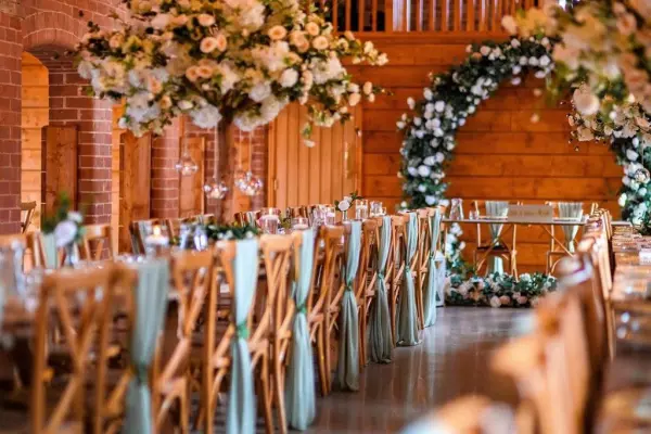Spacious barn interior with rustic wooden beams, elegant floral arrangements, and beautifully set tables adorned with soft blue accents.