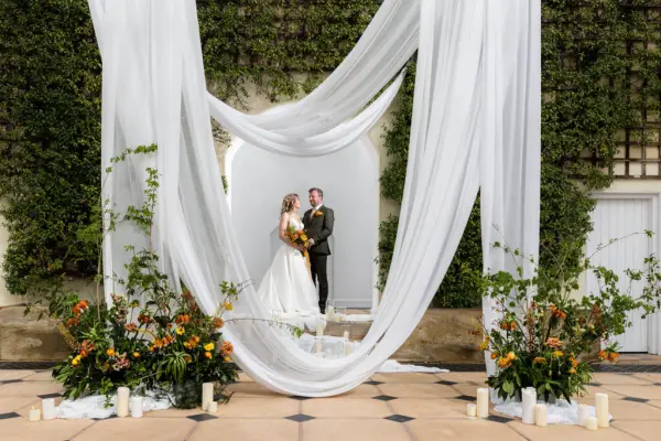 Elegant outdoor ceremony space featuring flowing white drapery, vibrant floral arrangements, and a stone backdrop for a romantic wedding.