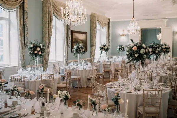 Elegant ballroom featuring crystal chandeliers, round tables adorned with floral centerpieces, and soft drapery, perfect for a romantic wedding.