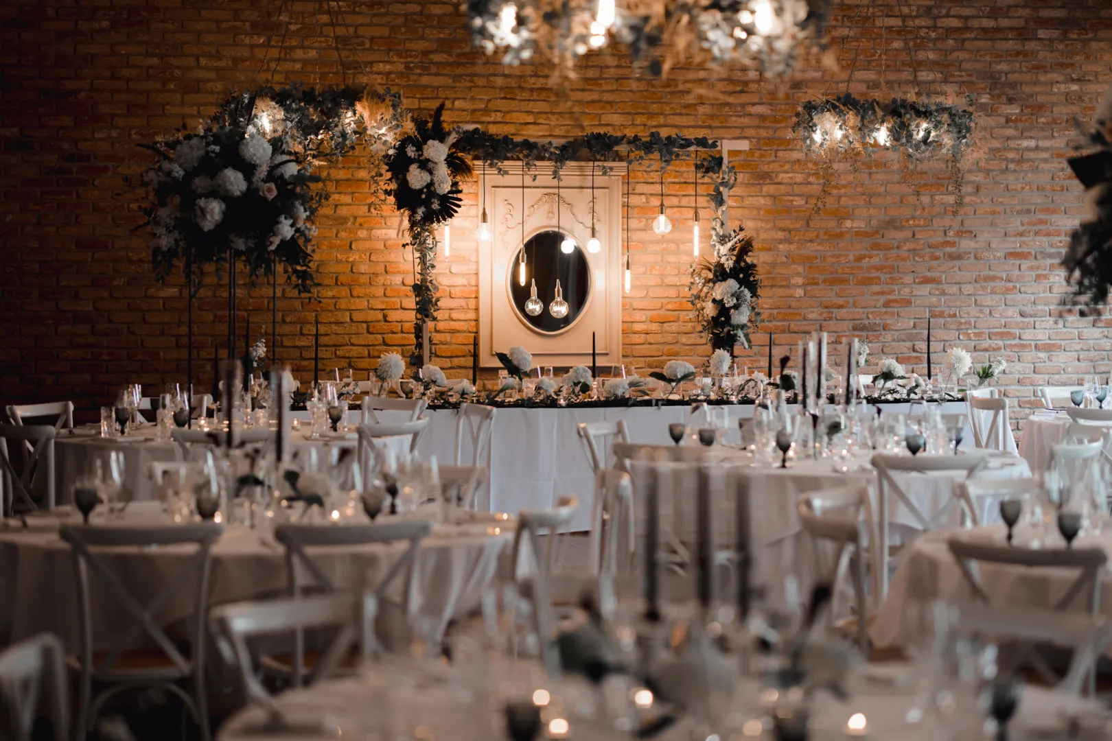 Charming reception space with elegant tables set for a wedding, adorned with floral arrangements and atmospheric hanging lights.