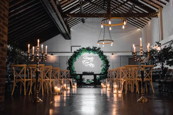 A charming indoor wedding venue featuring a rustic ceiling, elegant seating, greenery accents, and warm candlelight for an intimate ceremony.