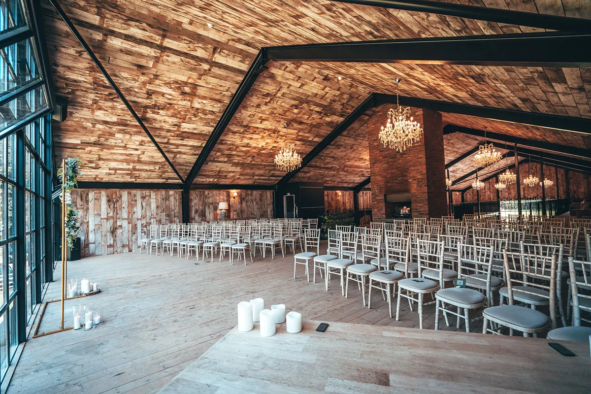 Rustic wedding venue featuring a spacious ceremony area with elegant chandeliers, wooden beams, and rows of chiavari chairs.