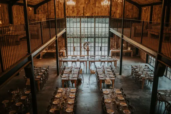 Spacious rustic barn venue featuring elegant wooden tables, exposed beams, and a large window for natural light, perfect for intimate gatherings.