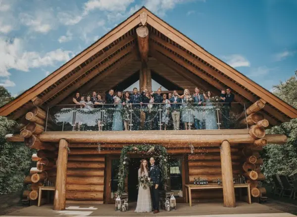 Charming log cabin venue featuring a spacious balcony, surrounded by lush greenery, perfect for a rustic wedding celebration with family and friends.