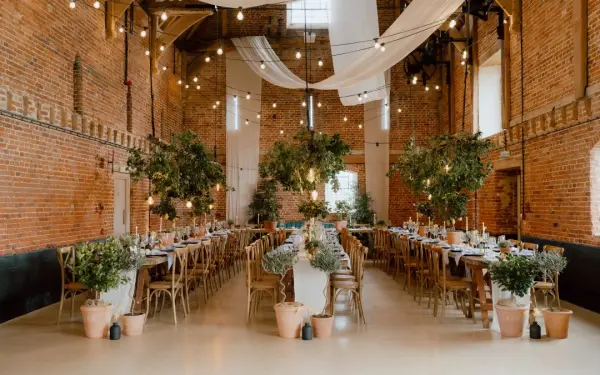 An intimate reception space featuring rustic brick walls, elegant string lights, and tables adorned with greenery and floral arrangements.