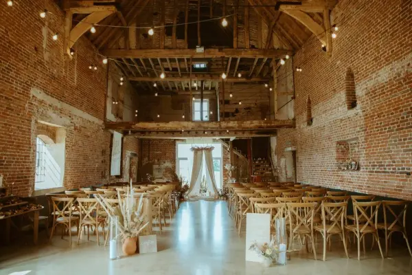 Rustic barn interior with exposed brick walls, wooden beams, and string lights, featuring elegant seating and a warm, inviting atmosphere.