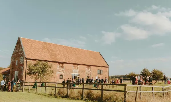 Charming rustic barn surrounded by greenery, hosting a lively outdoor wedding ceremony with guests enjoying the beautiful day.