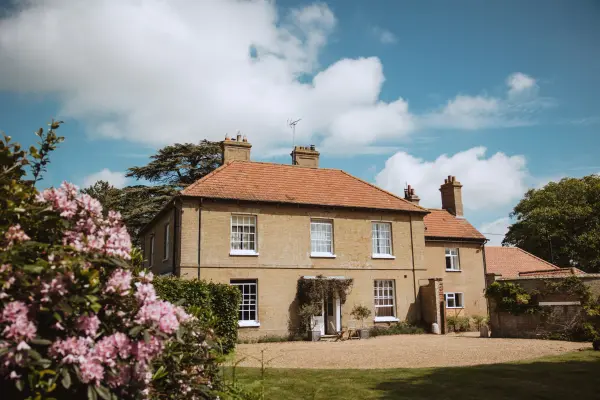 Charming countryside house with a warm exterior, surrounded by lush greenery and vibrant pink flowers, perfect for an intimate wedding setting.