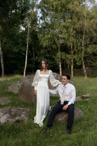 A couple poses in a serene outdoor setting with lush greenery and large rocks, capturing a natural, romantic wedding vibe.