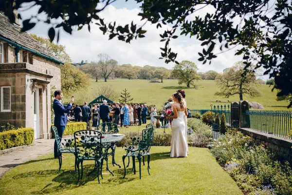 A scenic outdoor space featuring lush greenery, elegant seating, and a joyful couple surrounded by guests celebrating their wedding.