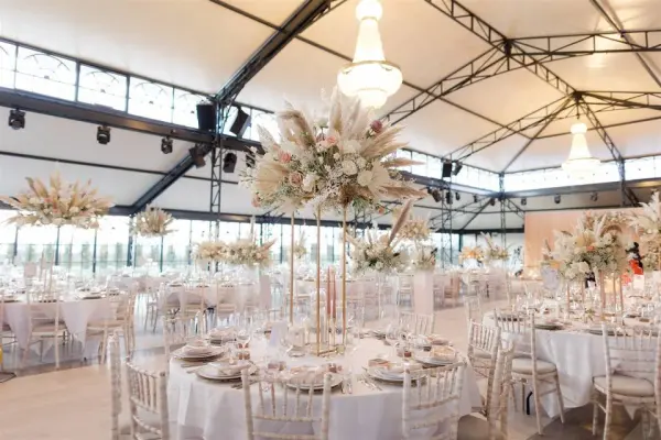 Elegant indoor reception space featuring high ceilings, tall floral centerpieces, and round tables set for a romantic wedding celebration.