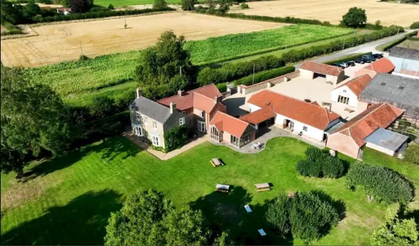 Charming venue featuring a spacious green lawn, rustic buildings, and scenic fields, perfect for an outdoor wedding celebration.