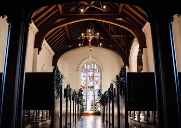 Charming church interior featuring wooden beams, rows of pews, and a stunning stained glass window at the end, perfect for intimate ceremonies.