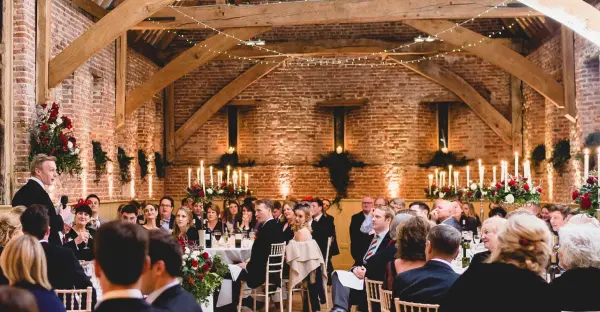 Rustic barn wedding venue featuring exposed brick, wooden beams, candlelit tables, and floral accents, creating an intimate ambiance.
