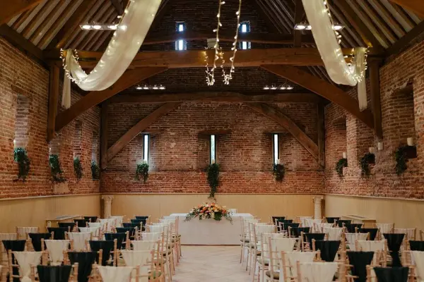 Charming rustic barn with exposed brick walls, wooden beams, and elegant lighting, set for a wedding ceremony with chairs and floral decor.