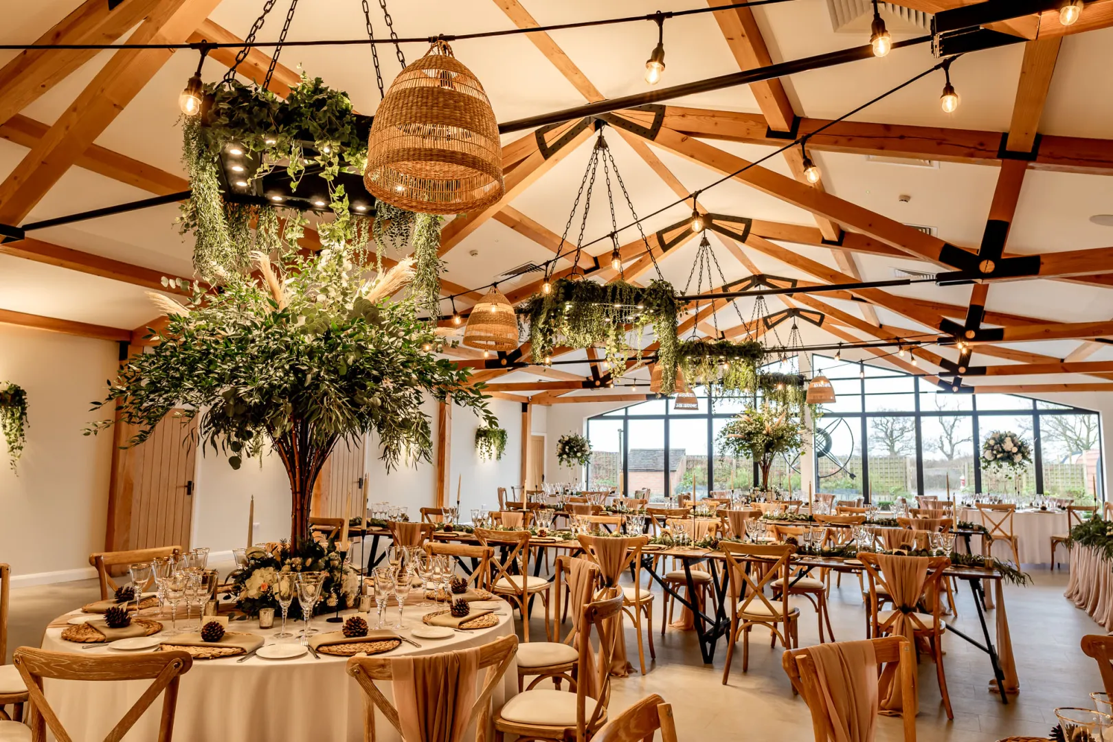 Elegant reception hall featuring wooden beams, lush greenery, and stylish decor, perfect for creating a romantic wedding atmosphere.