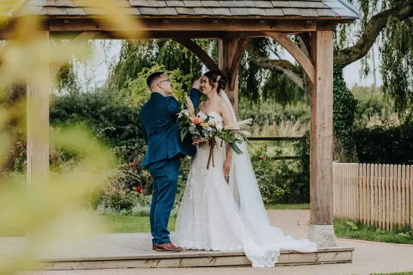 Couple sharing a romantic moment under a stunning wooden gazebo, surrounded by greenery and a charming garden setting.