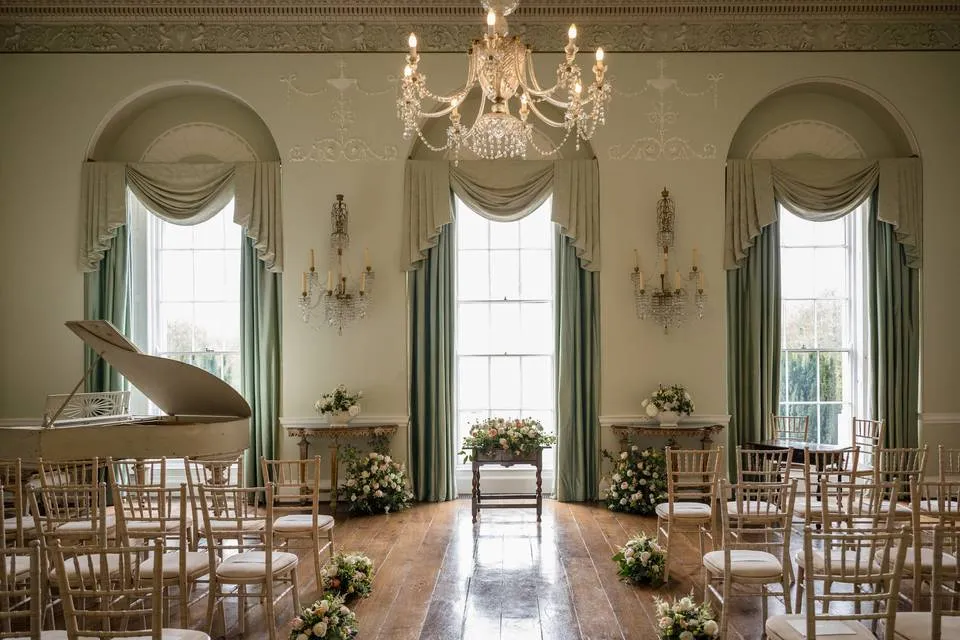 Elegant ceremony space featuring large windows, chandelier, hardwood floors, and beautifully arranged floral accents. Chic and stylish atmosphere.
