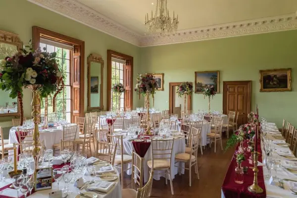 Elegant reception area with large windows, ornate mirrors, and beautifully set tables adorned with floral centerpieces and fine dining ware.