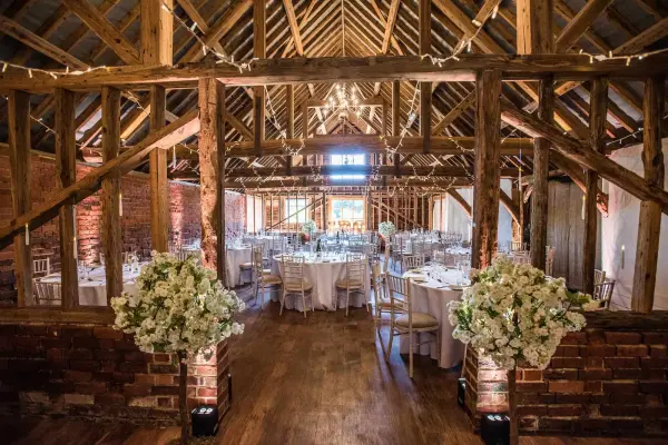 Rustic barn venue featuring exposed wooden beams, elegant round tables, and floral arrangements, creating a charming reception atmosphere.