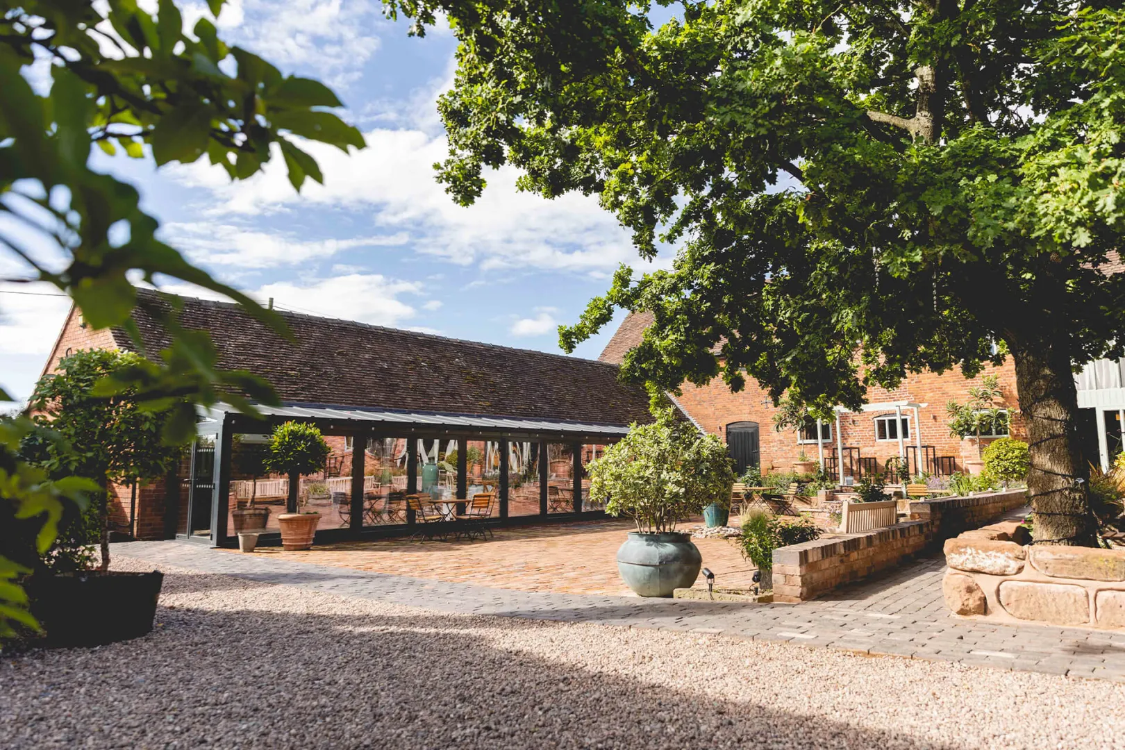 Charming outdoor courtyard with a rustic stone building, lush green trees, and landscaped flower pots, perfect for a scenic wedding celebration.