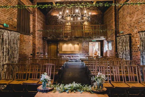 Charming rustic ceremony space with exposed brick walls, wooden seating, and a stunning chandelier overhead, perfect for intimate weddings.