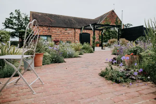 Charming brick pathway leading to a rustic barn, surrounded by vibrant flowers and greenery, perfect for an outdoor wedding celebration.