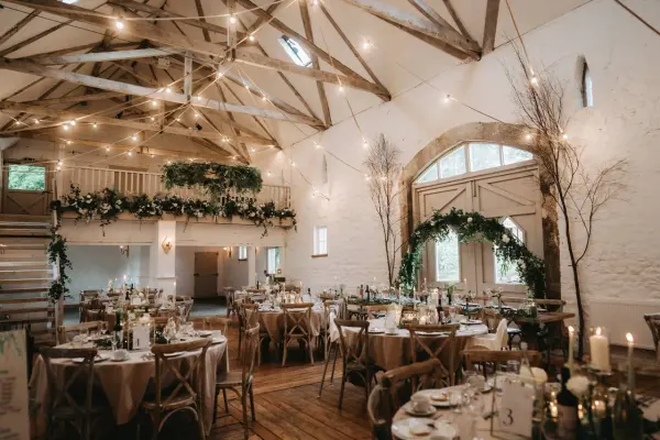 Charming rustic barn with soaring ceilings, wooden beams, elegant tables, and romantic string lights, perfect for a cozy wedding reception.