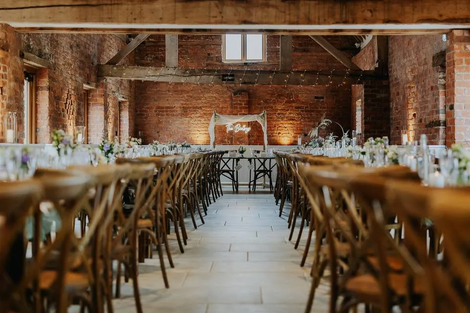Rustic barn venue featuring exposed brick walls, wood beams, and elegant long tables adorned with floral centerpieces for a cozy reception.