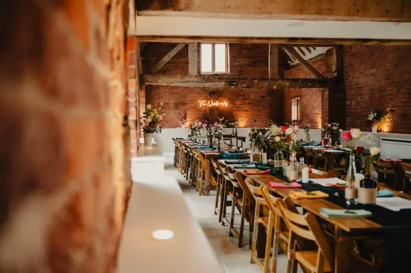 Rustic brick walls frame a charming reception area with long wooden tables adorned with vibrant flowers and elegant table settings.