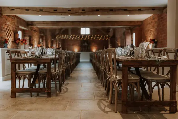 Rustic banquet hall featuring wooden cross-back chairs, warm brick walls, and softly lit ambiance, perfect for intimate wedding receptions.