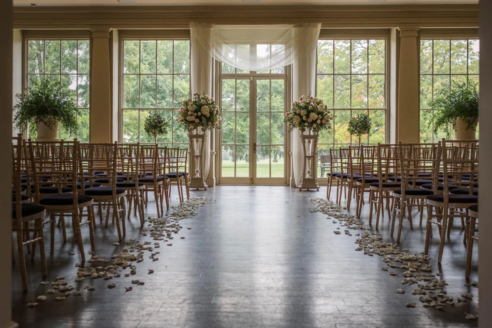 Elegant indoor ceremony space featuring rows of chairs, floral arrangements, and natural light streaming through large windows.