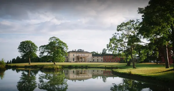 Idyllic venue featuring a grand estate reflected in a serene lake, surrounded by lush greenery and mature trees. Perfect for outdoor ceremonies.