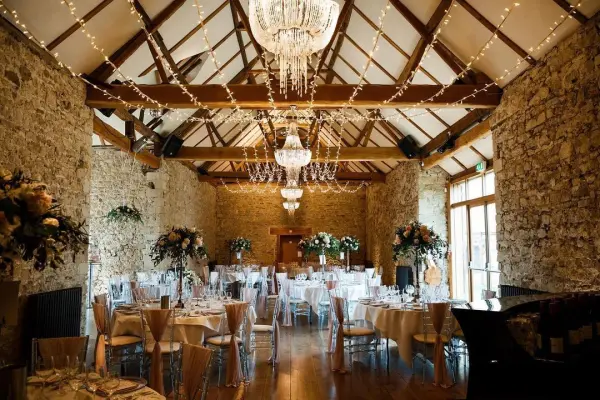 Rustic venue with exposed stone walls, crystal chandeliers, and elegant tables set for a wedding reception, creating a warm, inviting atmosphere.