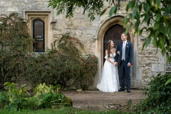 A couple stands joyfully outside a rustic stone entrance, framed by lush greenery—ideal for intimate wedding portraits.
