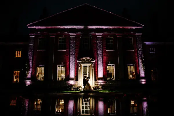 Elegant mansion illuminated at night, reflecting in water, creating a romantic backdrop for a couple's private moment.