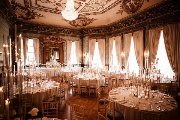 Elegant ballroom featuring ornate decor, large windows, and beautifully arranged tables with shimmering candlelight for a romantic wedding setting.