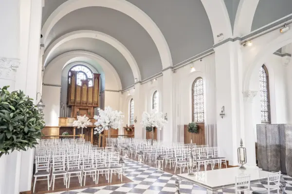 Elegant ceremony space featuring white chairs, tall floral arrangements, and a stunning arched ceiling with vintage organ backdrop.