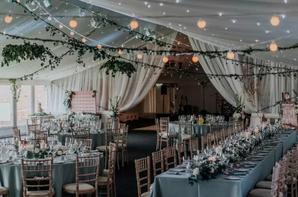 Elegant reception space with draped fabric, twinkling lights, and tables adorned with lush floral centerpieces. A charming atmosphere for celebrations.